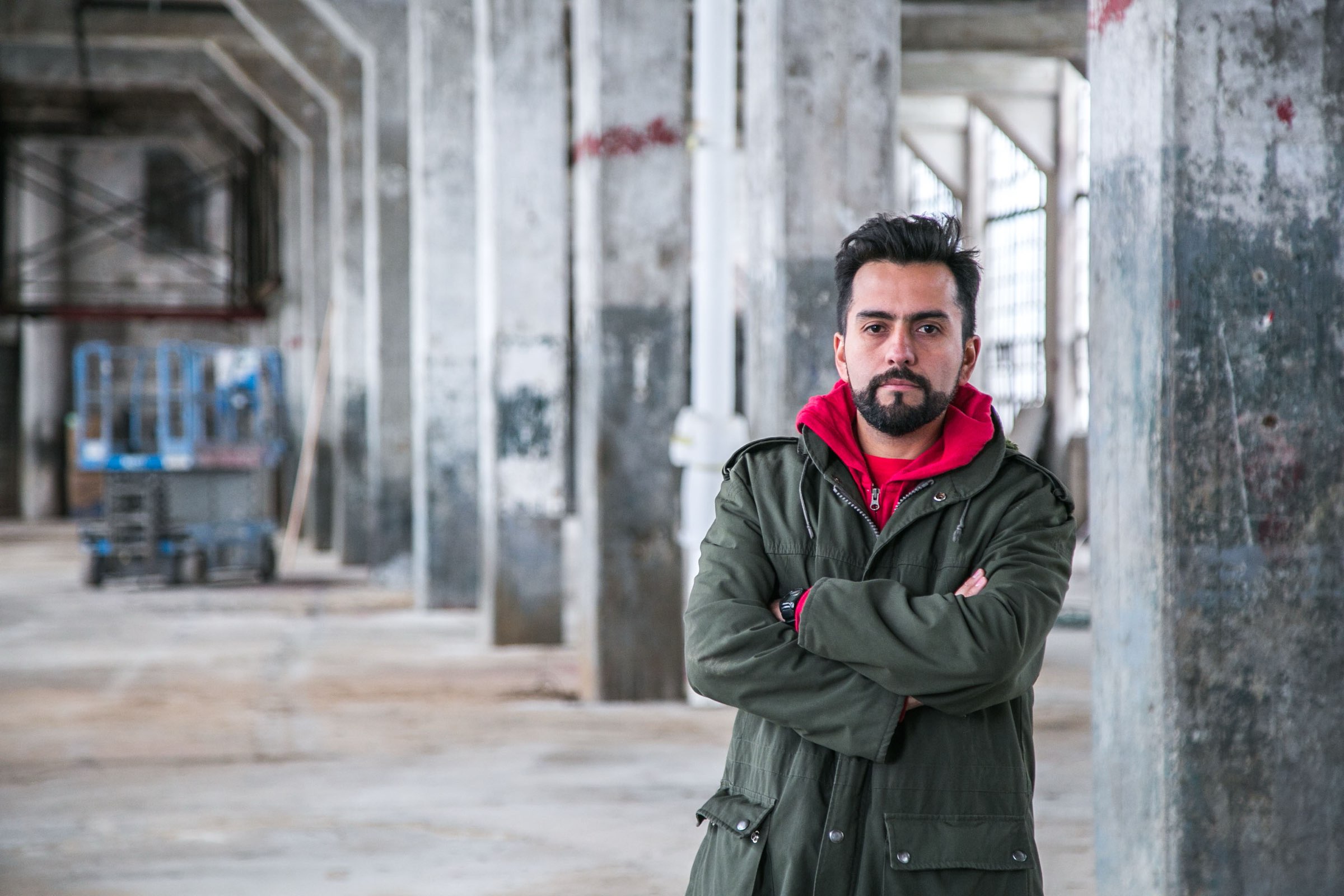 Jorge Cubillos in an empty concrete hall, arms crossed, green parka over a red hoodie